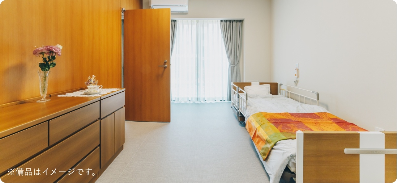 介護施設の居室。木製家具とベッド、採光窓が配置された広々とした空間