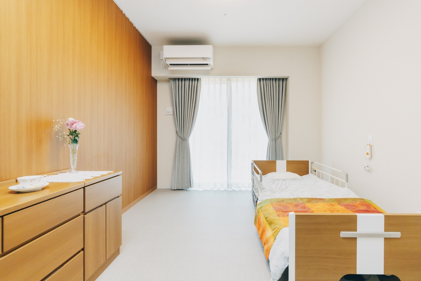 木調のモダンな個室。ベッド、ドレッサー、エアコン、窓からの採光が備わる。
