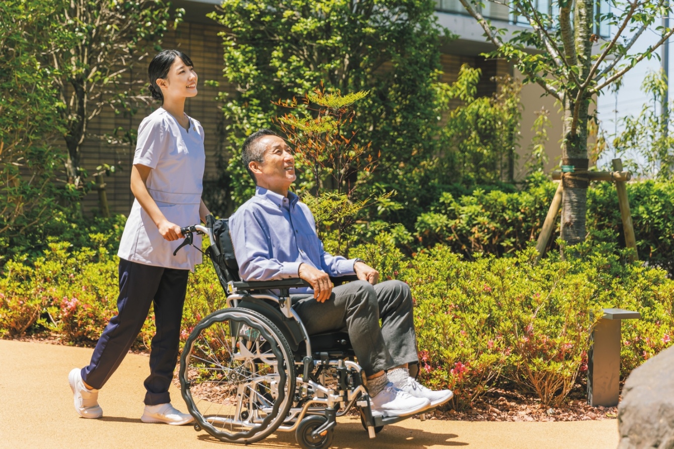 介護職員が車椅子利用者の屋外散歩をサポートしている様子